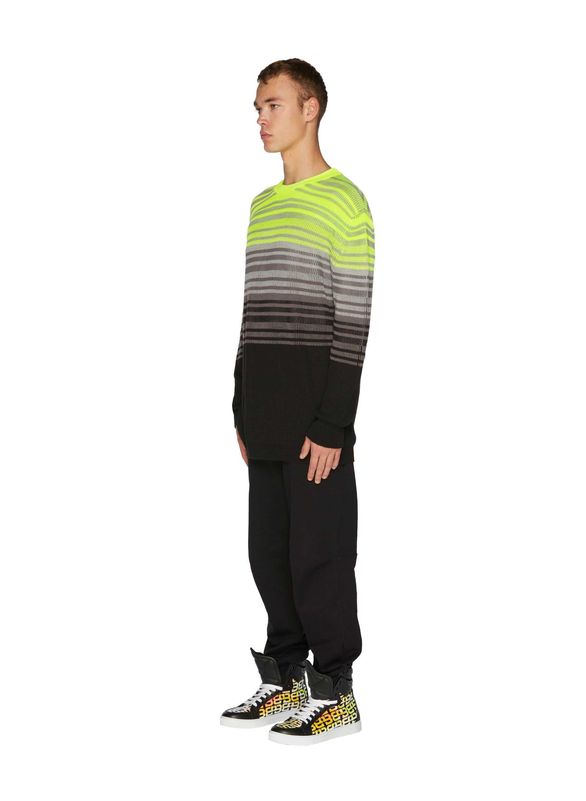 Model in a Knit Fluo Crewneck featuring neon yellow and gray tones, paired with black joggers and 3D Logo Iridescent Sneakers